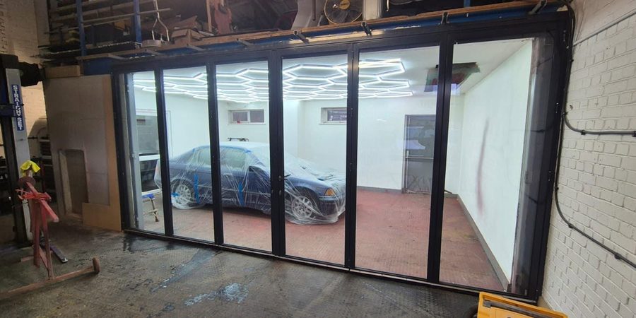 The bifold glazing at J's P8WORX workshop, clean enough to see the car being prepped behind it.