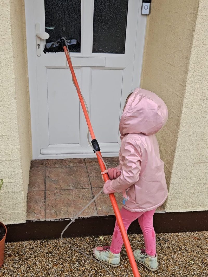 Jay's young daughter cleaning a front door with a water-fed pole.
