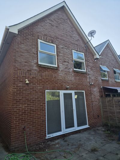 The rear of a brick house before cleaning, windows and frames dulled.