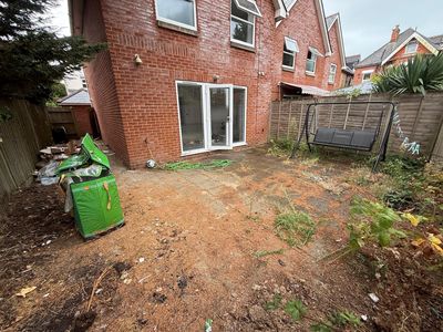 A rear patio overgrown with weeds and slabs buried under dirt and pine needles.