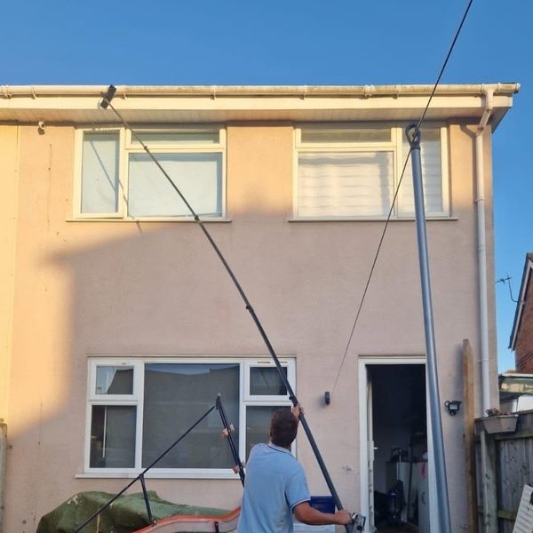Cleaning the rear windows of a house with a pole.