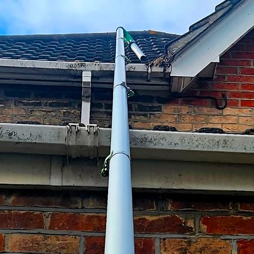 A gutter vacuum reaching a blocked gutter from the ground.